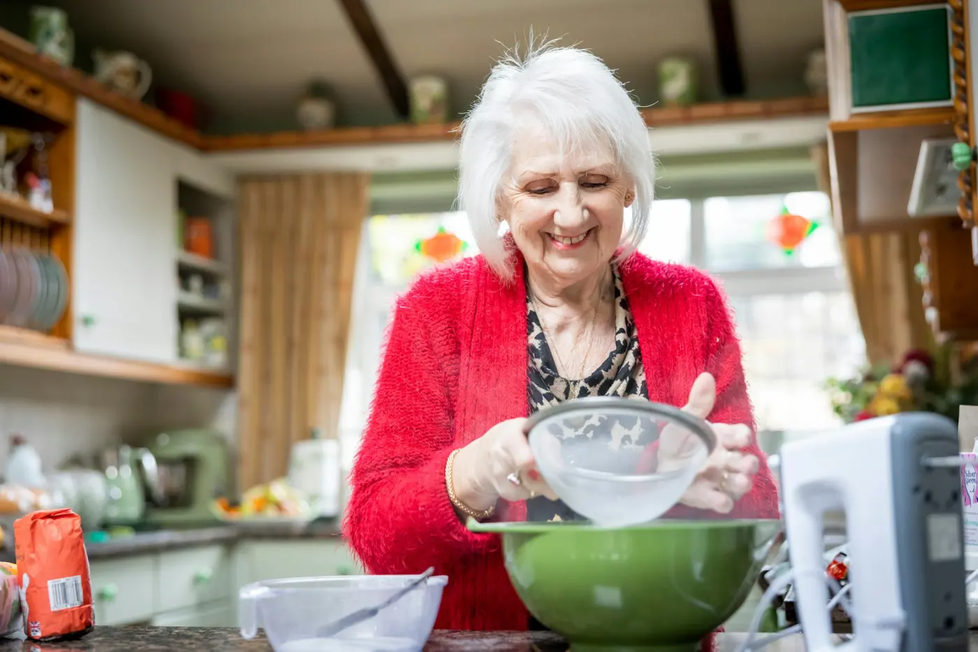 An older woman smiling as she mixes a bowl in her kitchen