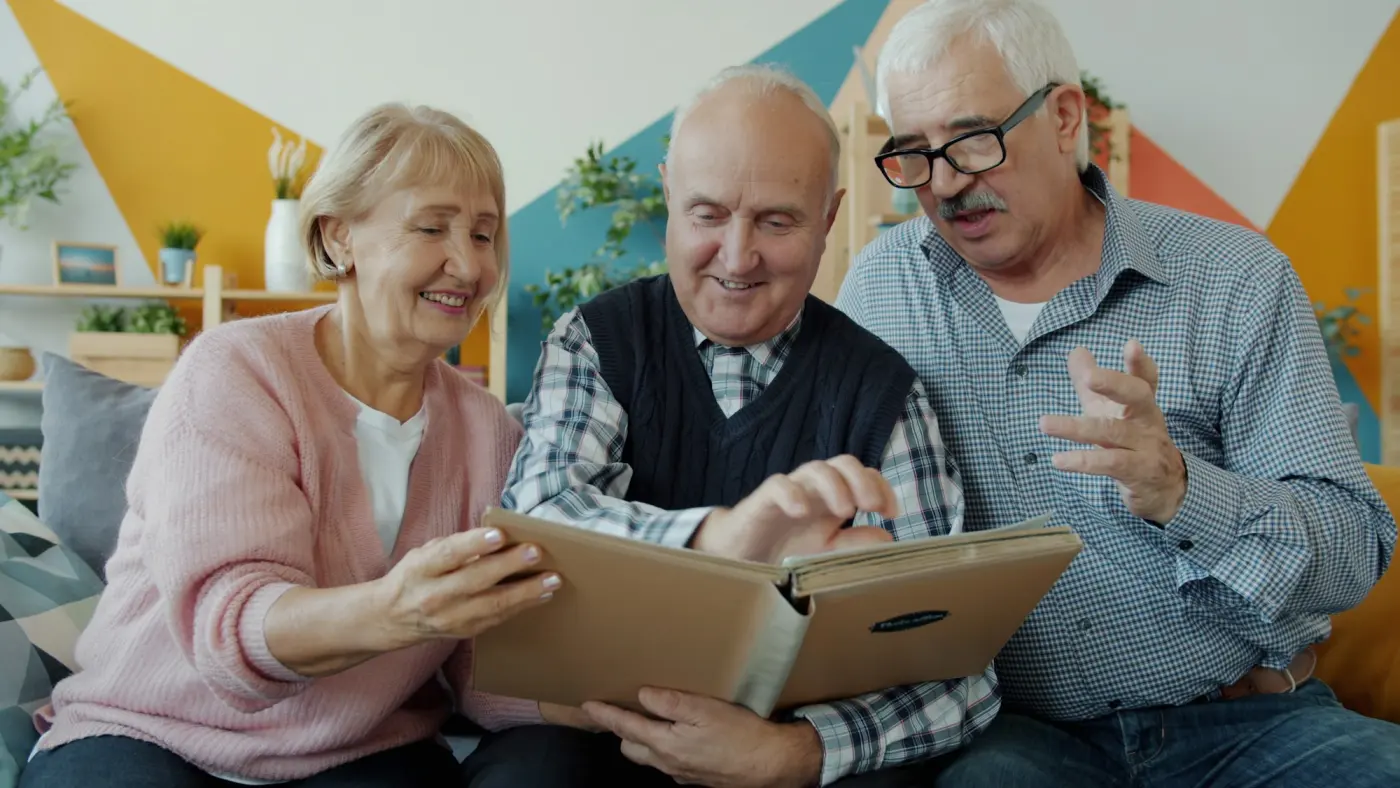 Three older friends laughing together over a photo album